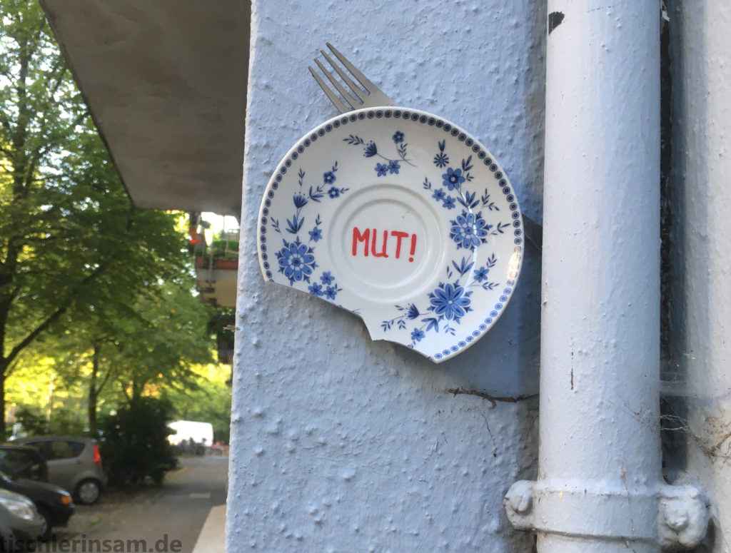 Mut! geschrieben in roten Großbuchstaben auf einem Teller mit Zwiebelmuster in Blau, der an einer Hauswand befestigt ist. Streetart in Hamburg. Künstler*in: Frau Jule, Fotografiert von Sam